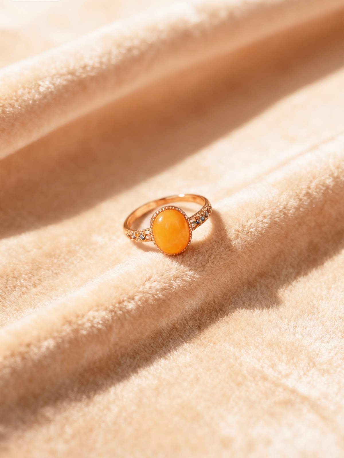Verdant Vine amber ring resting on plush champagne fabric in sunlight