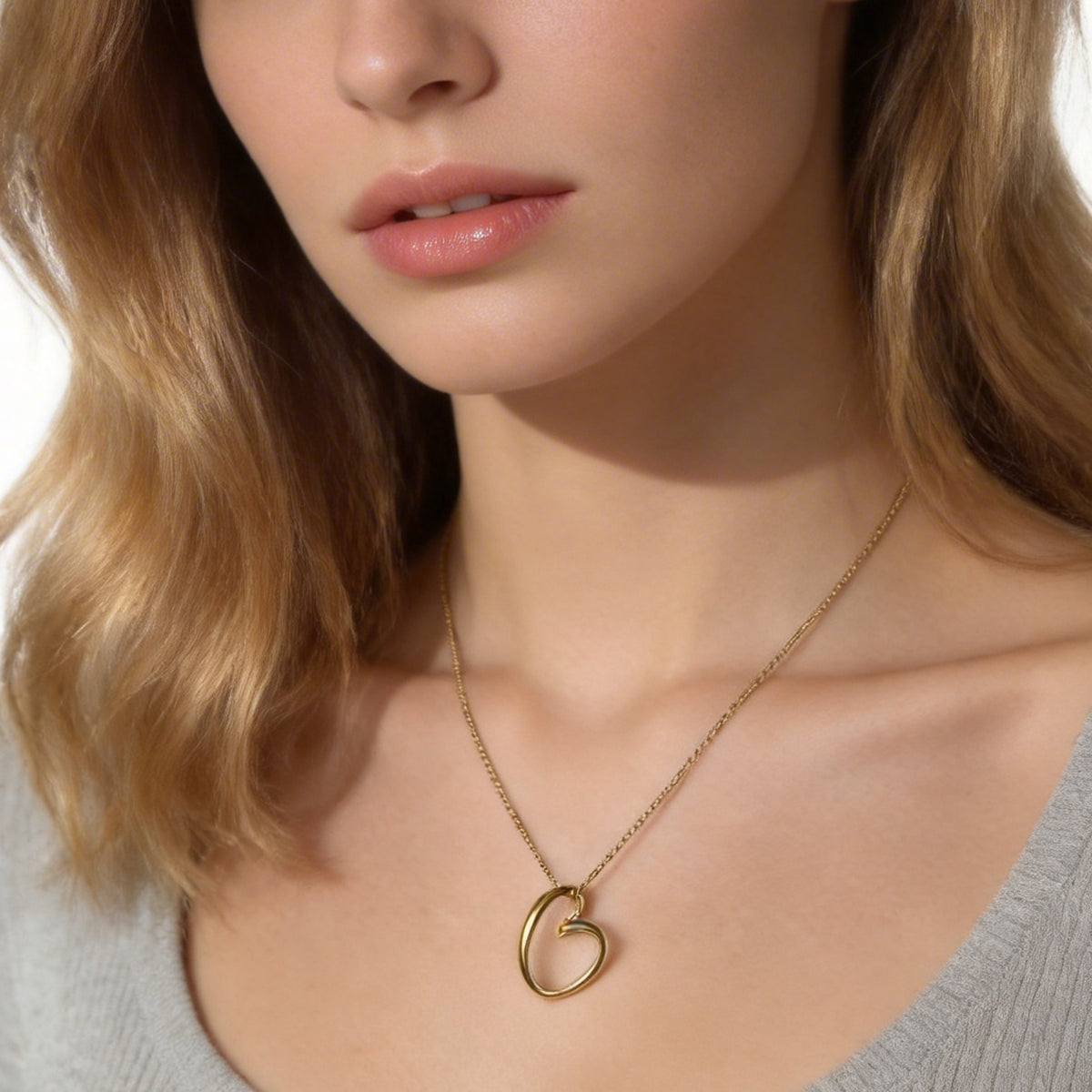 Close view of a gold heart-knot pendant above a white V-neck top