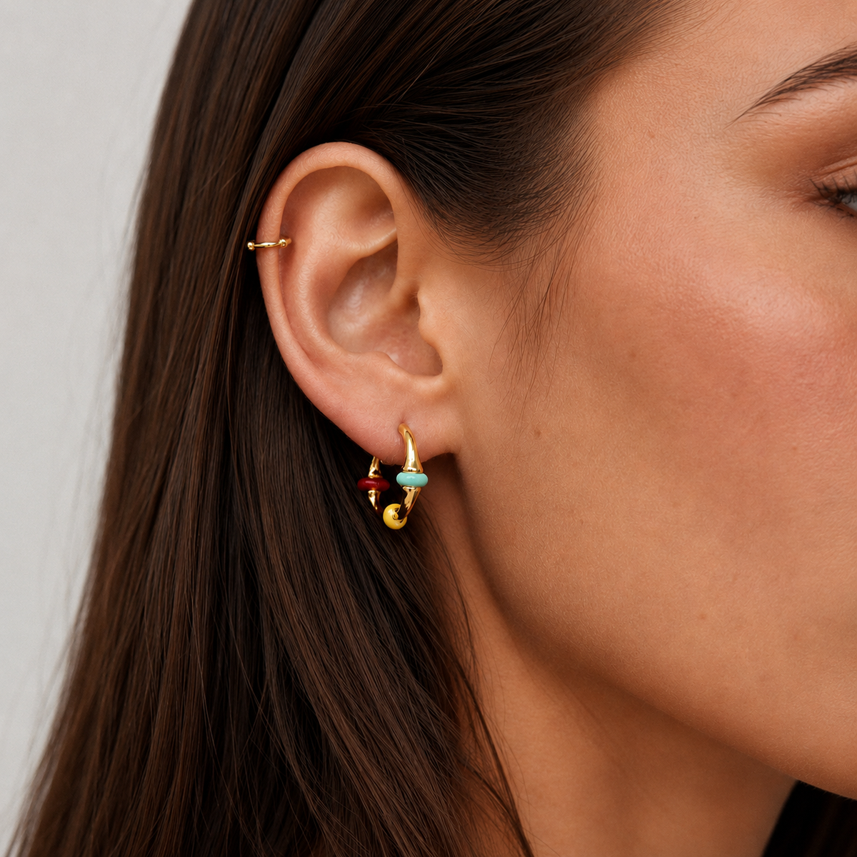 Close-up of a gold enamel clip-on hoop earring with turquoise, yellow and red accents worn on the earlobe