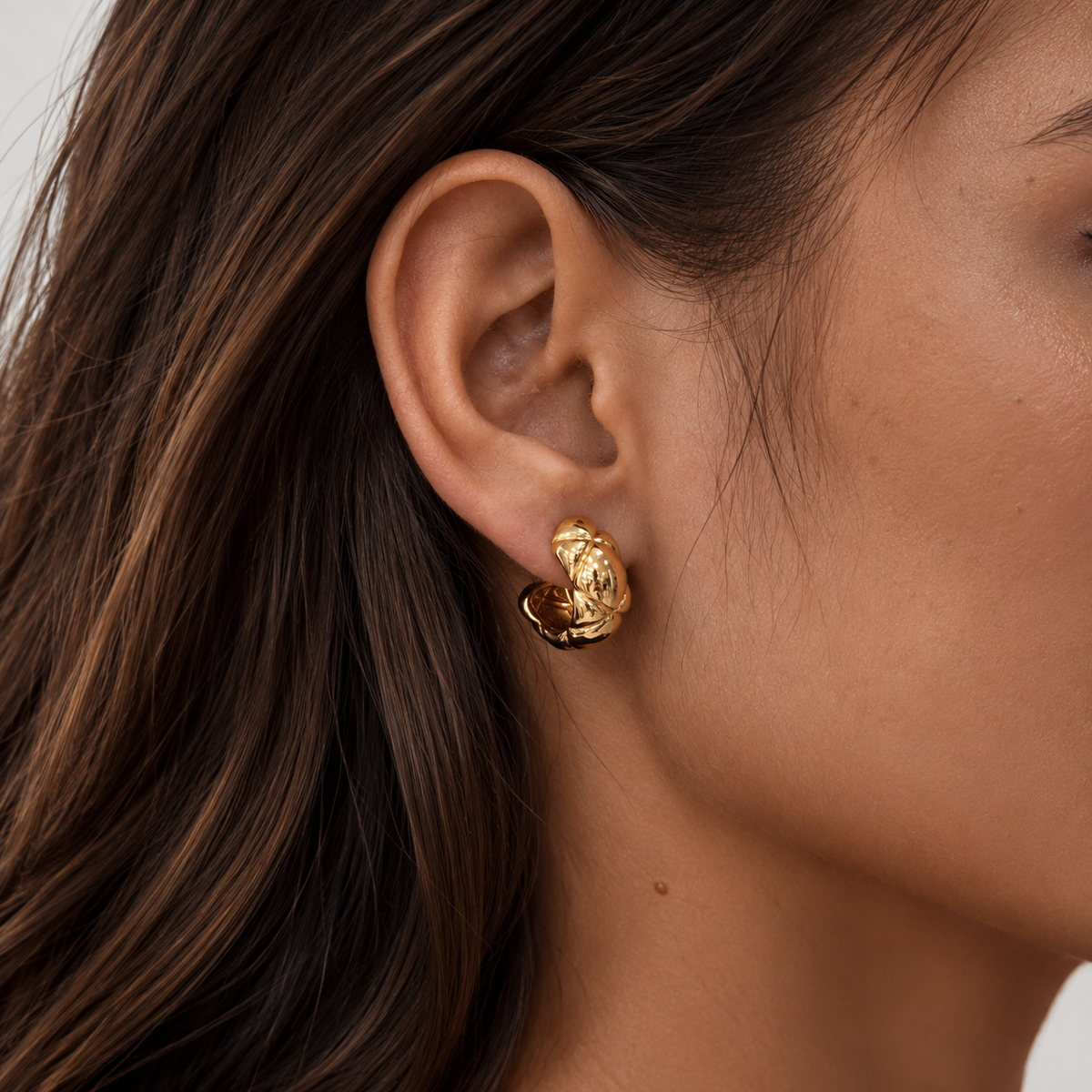 Close-up of a gold quilted dome clip-on hoop earring worn on the earlobe