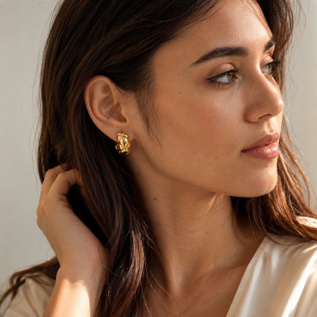 Model wearing a gold quilted clip-on hoop earring with a cream blouse in sunlight