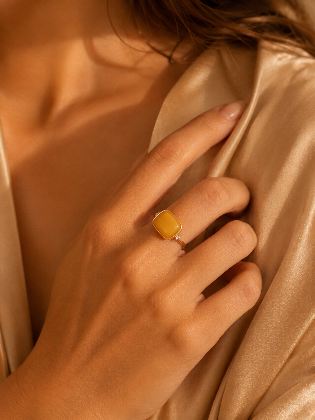 Sparkling Frame amber ring worn on a hand against warm champagne satin fabric