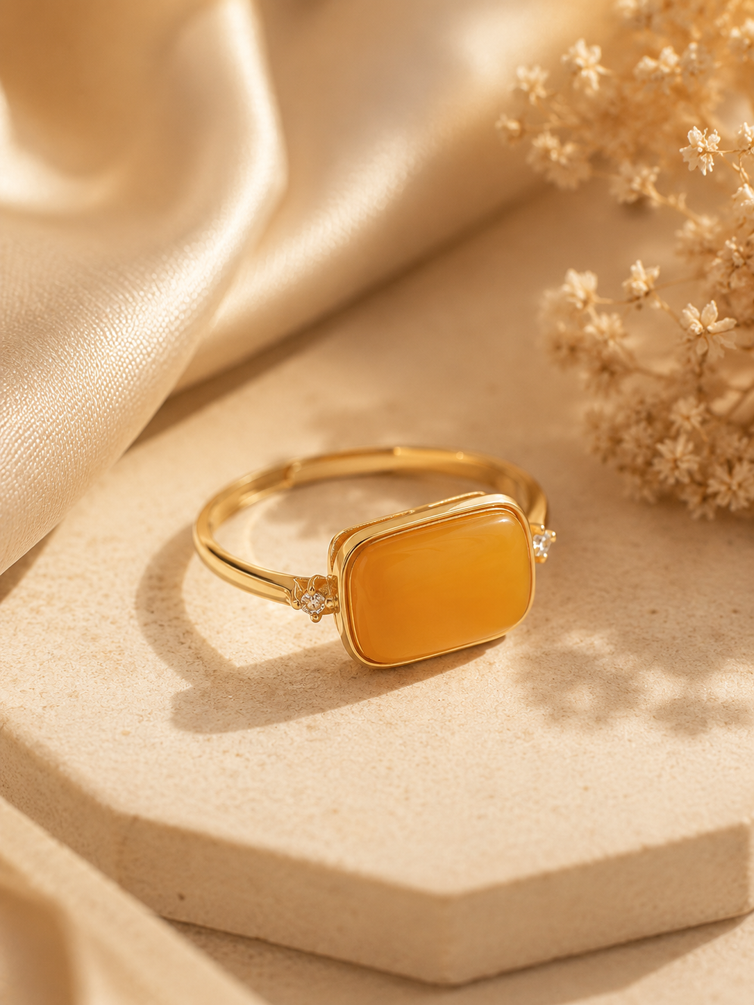 Sparkling Frame amber ring on a beige pedestal with dried flowers and golden satin