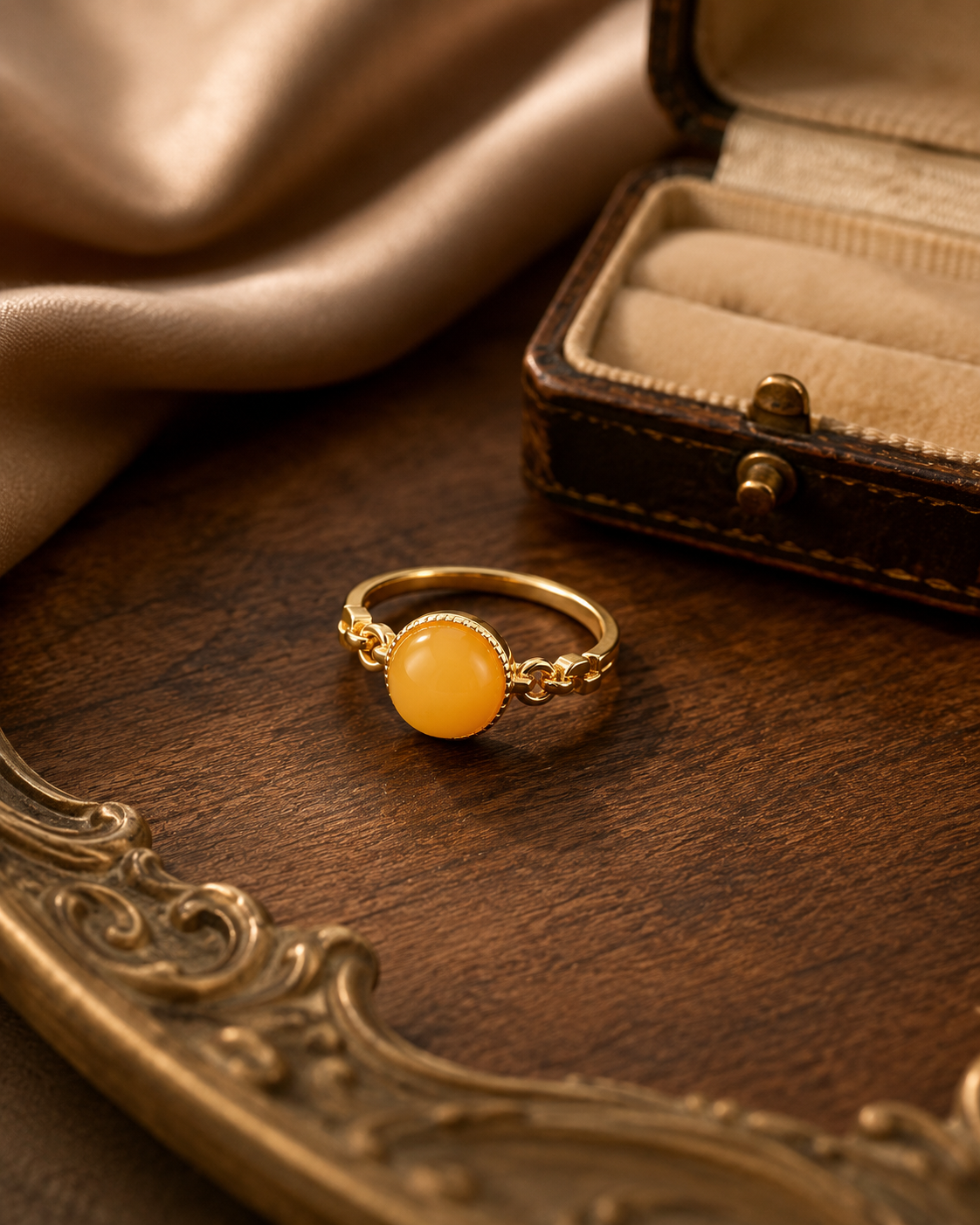 Braided Radiance amber ring beside a vintage jewelry box on dark wood