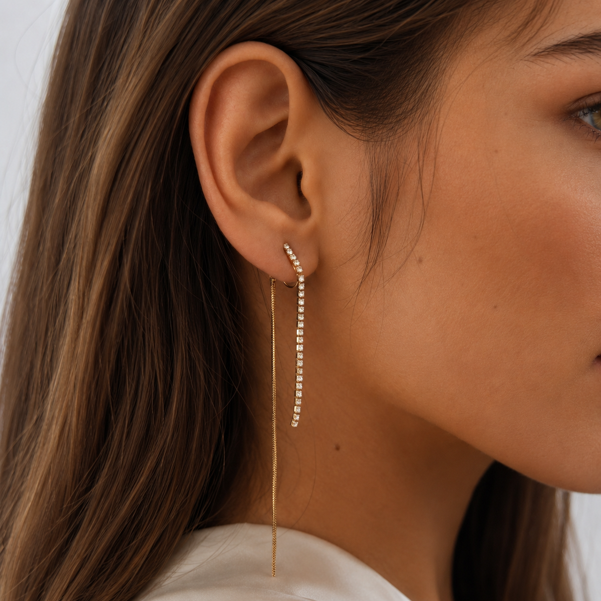 Close-up of a gold clip-on earring with a sparkling front chain and long rear tassels