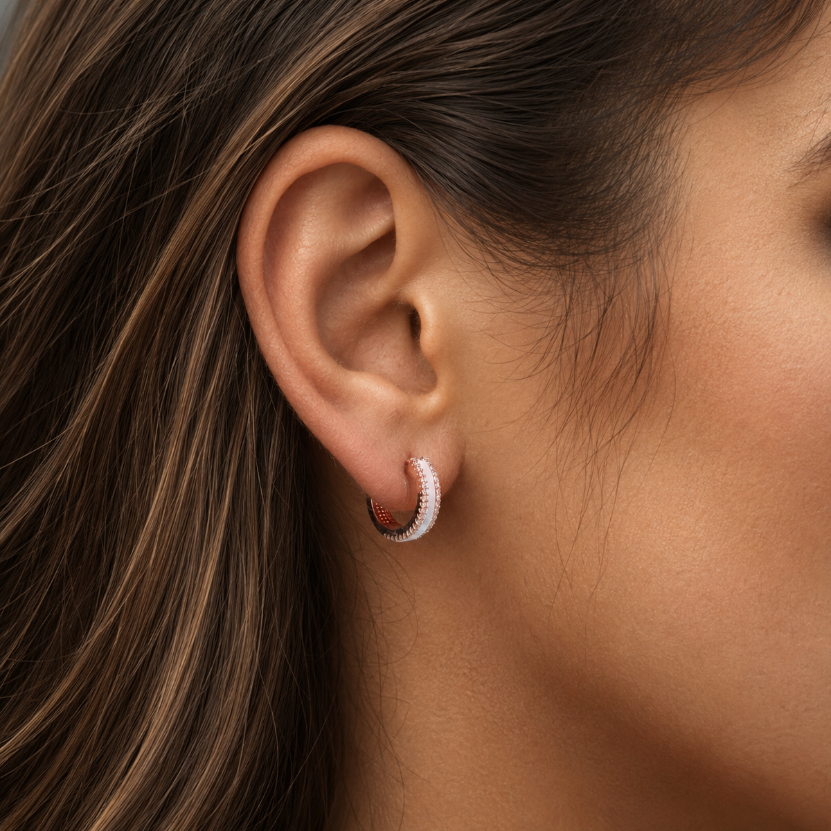 Close-up of a rose gold mother-of-pearl hoop with cubic zirconia worn on the ear