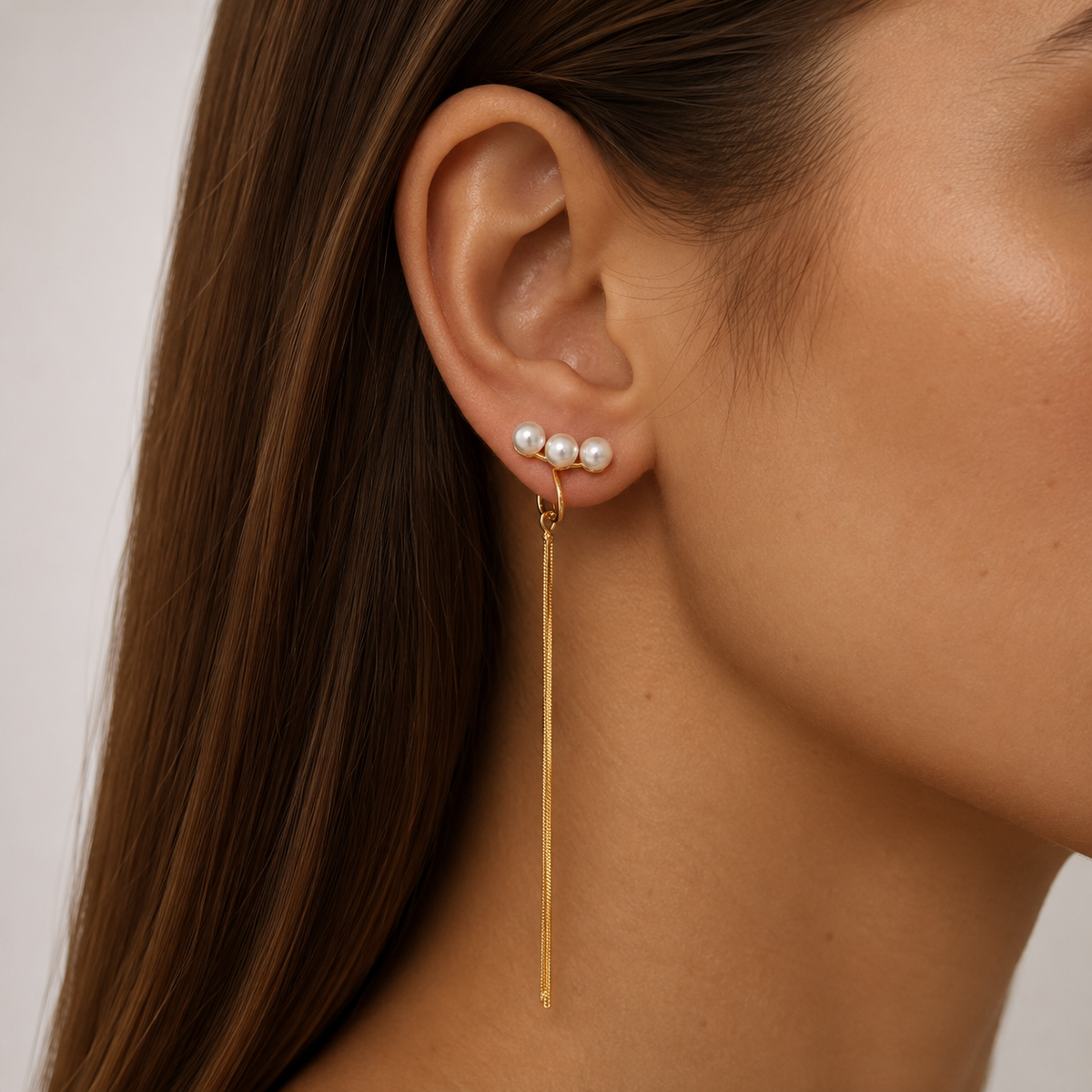 Close-up of SOMIY Triple Pearl Tassel Clip-On Dangle Earrings in gold worn on the ear