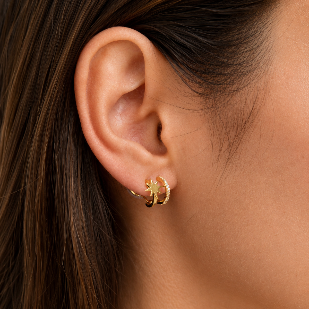 Gold starburst clip-on hoops worn on the ear, close-up