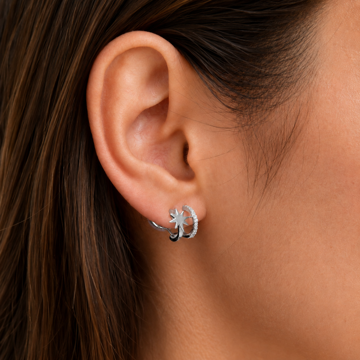Silver starburst clip-on hoops worn on the ear, close-up