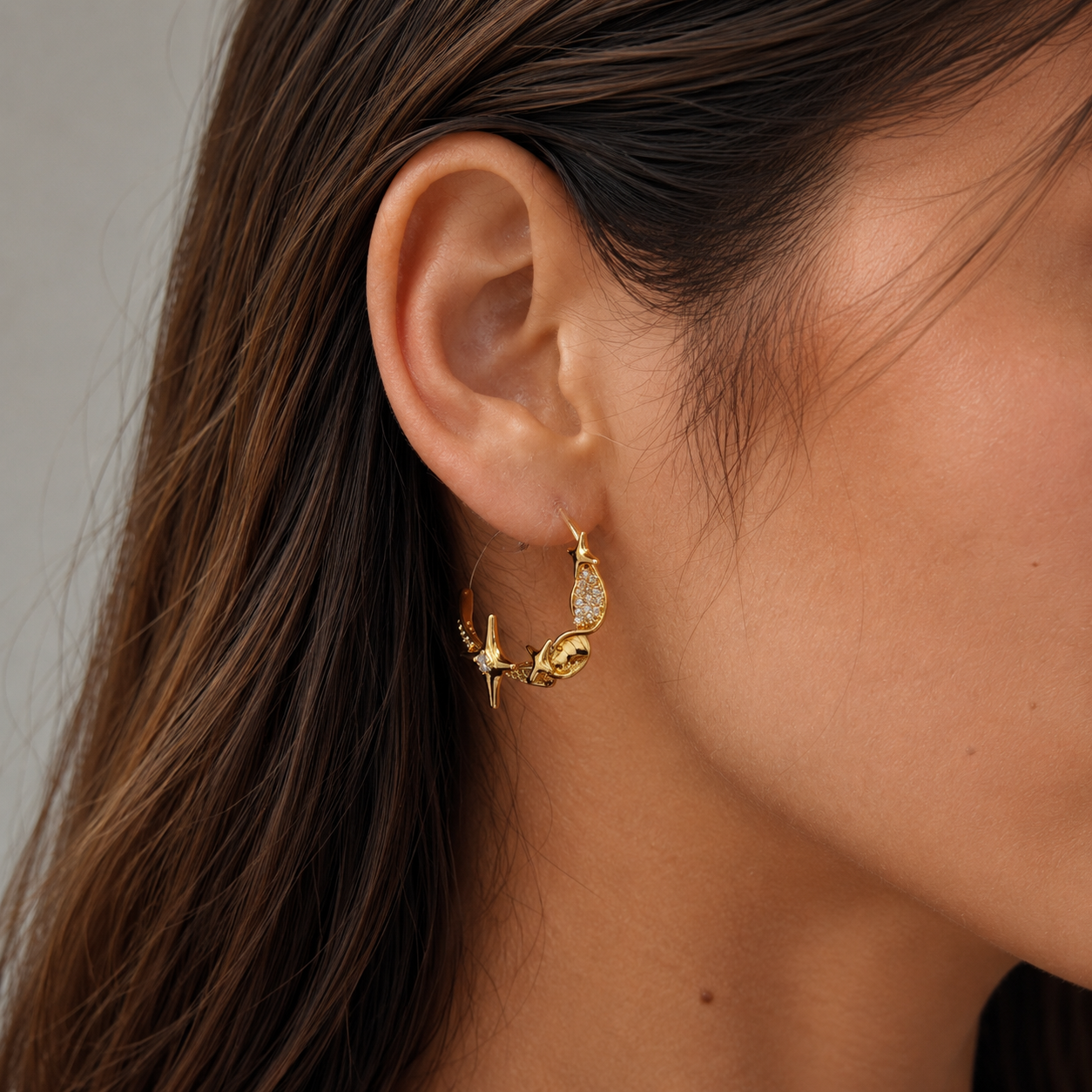 Close-up of a gold star and zircon twist clip-on hoop earring worn on the earlobe